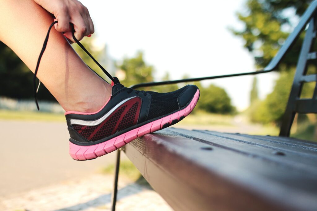 Su una panchina, una persona allaccia le scarpe da corsa, pronta per l'attività sportiva. Un gesto quotidiano che apre la strada a un momento di vitalità e benessere.